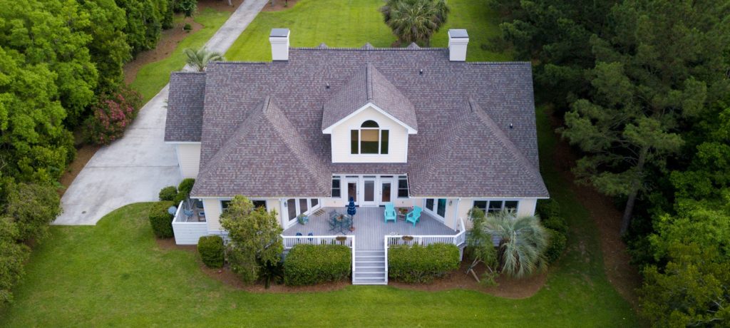 Aerial view of large home with new roof on wooded grassy propert